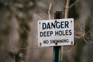 Close up of a warning sign against swimming due to deep holes, surrounded by dry branches. | Wade's Plumbing & Septic