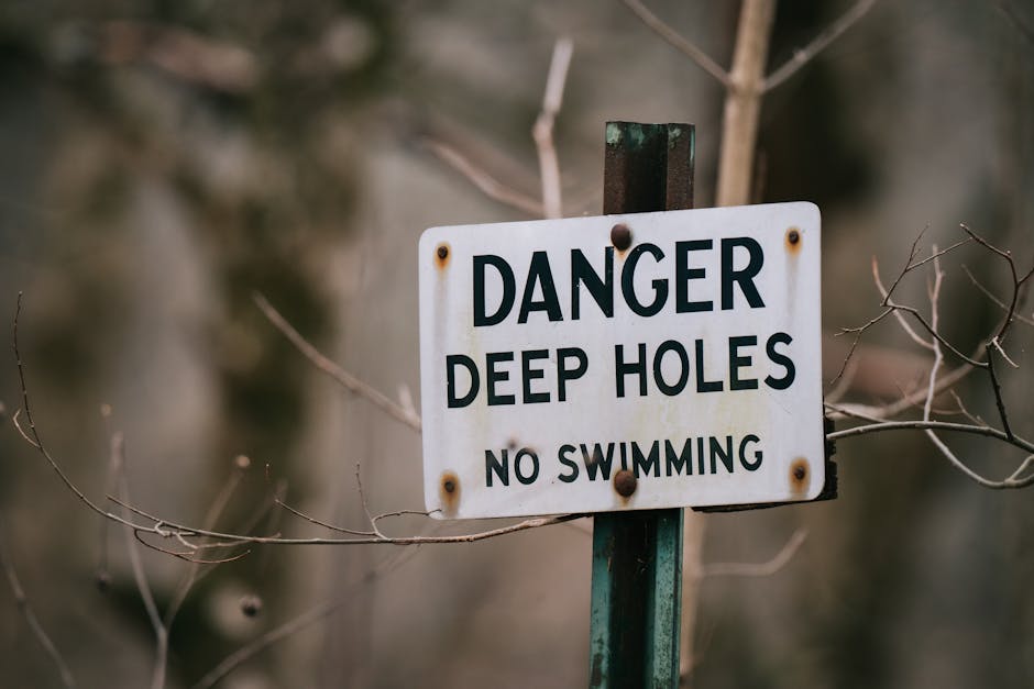 Close up of a warning sign against swimming due to deep holes, surrounded by dry branches. | Wade's Plumbing & Septic