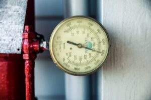 Detailed view of a pressure gauge attached to a red industrial pipe, measuring PSI and kPa. | Wade's Plumbing & Septic