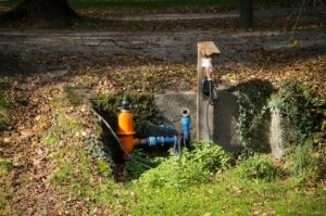 Water pipe system in a park with surrounding greenery and autumn leaves. | Wade's Plumbing & Septic