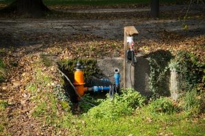 Water pipe system in a park with surrounding greenery and autumn leaves. | Wade's Plumbing & Septic