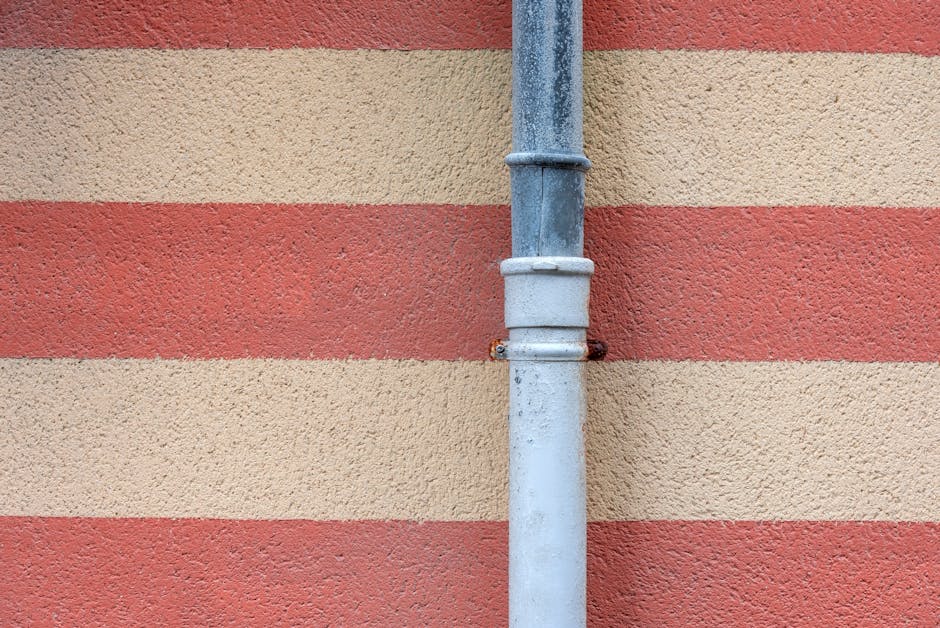 A metal drainpipe set against a red and beige striped textured wall. | Wade's Plumbing & Septic
